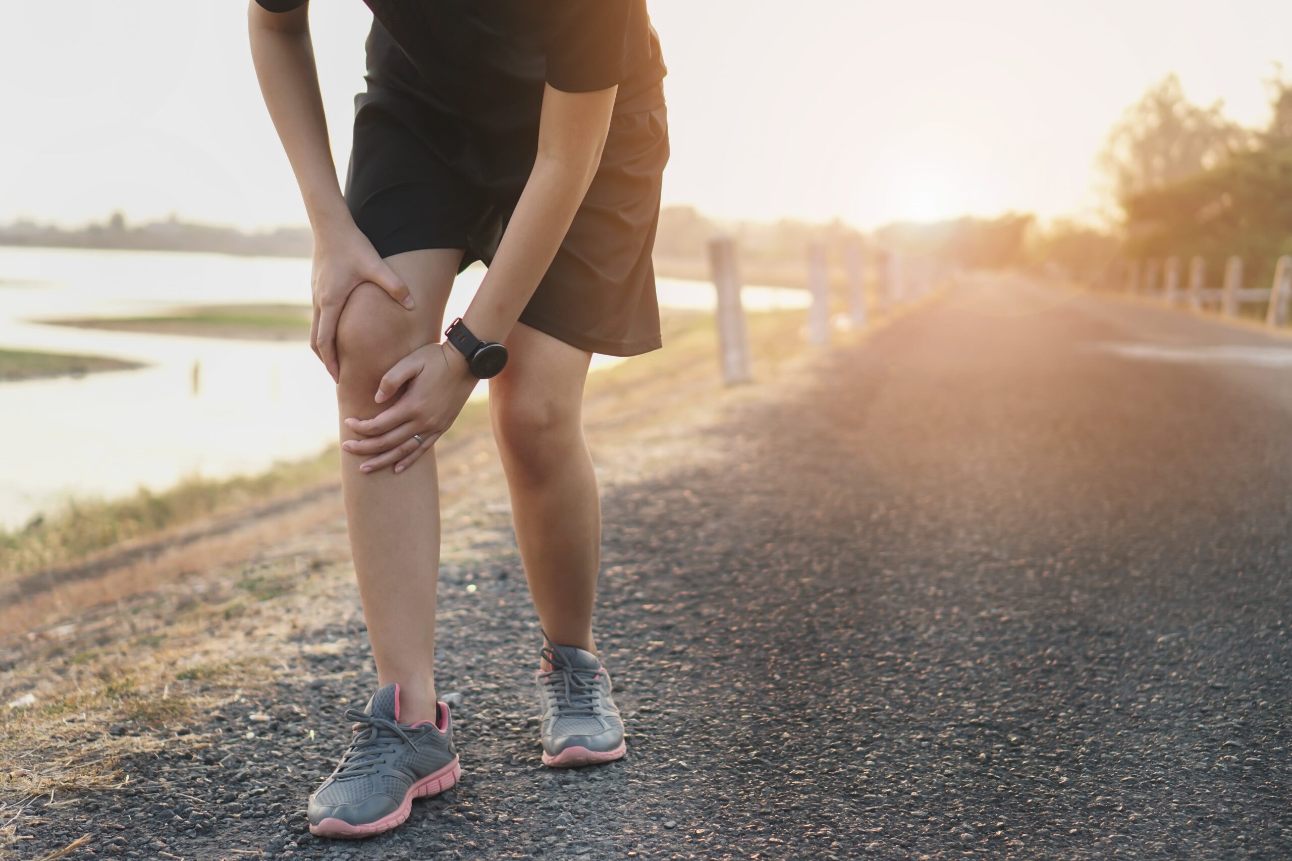 A person clutches their knee while standing on a running trail.