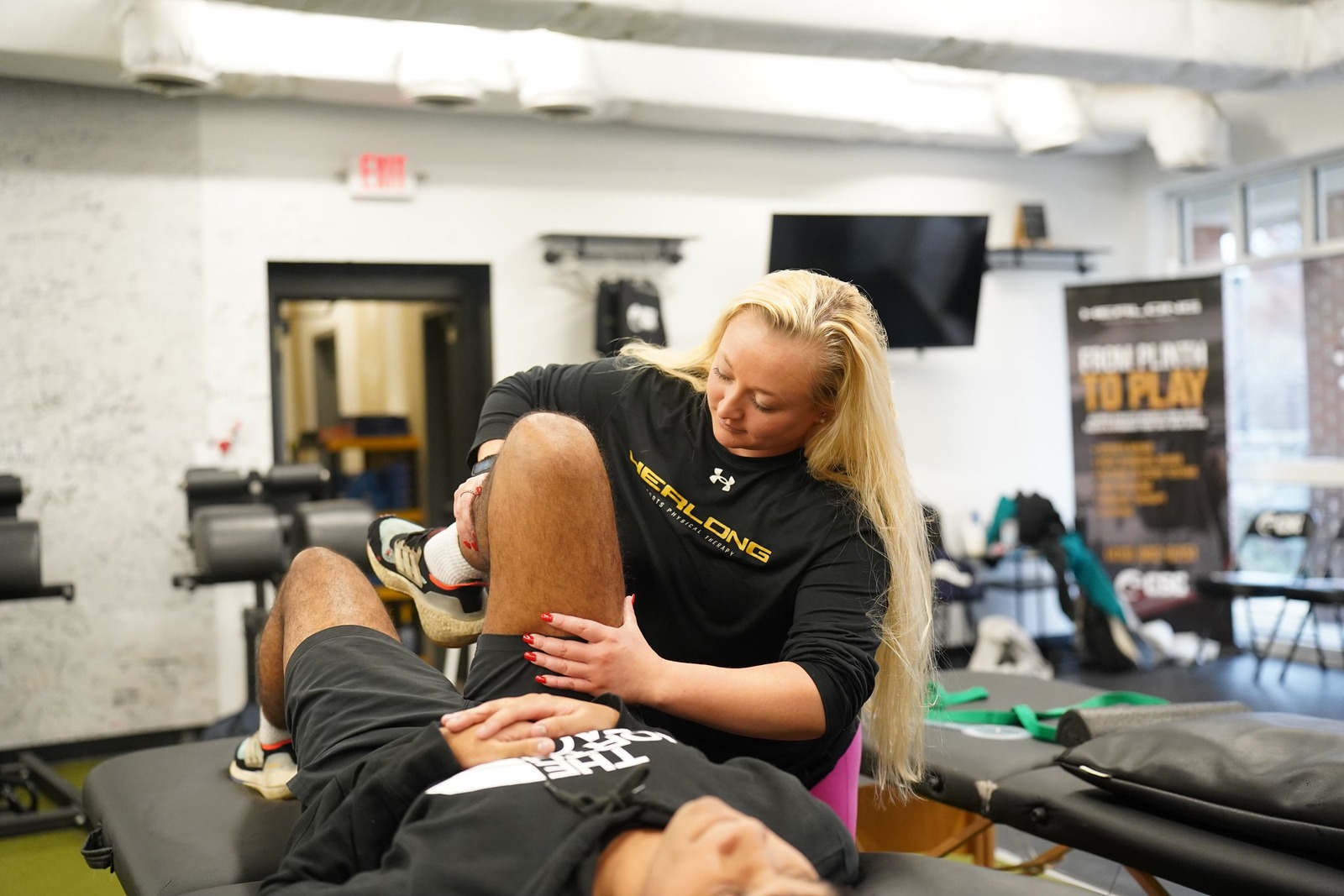 A female physical therapist bends the knee of a patient during a PT session.